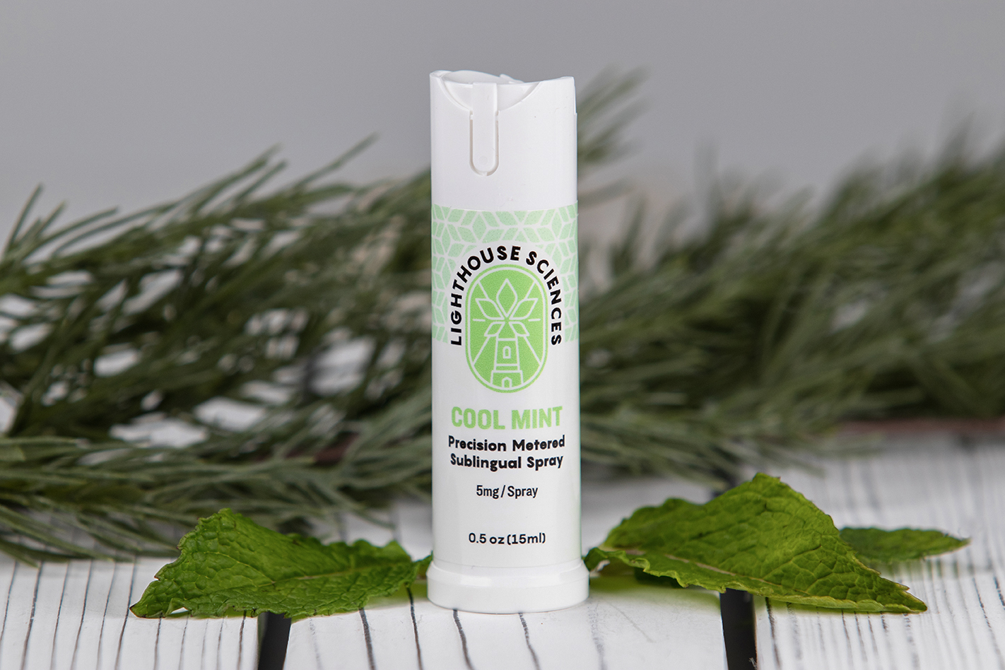 Lighthouse Sciences Cool Mint- Precision Metered Sublingual Spray Bottle surrounded by mint on a wood background