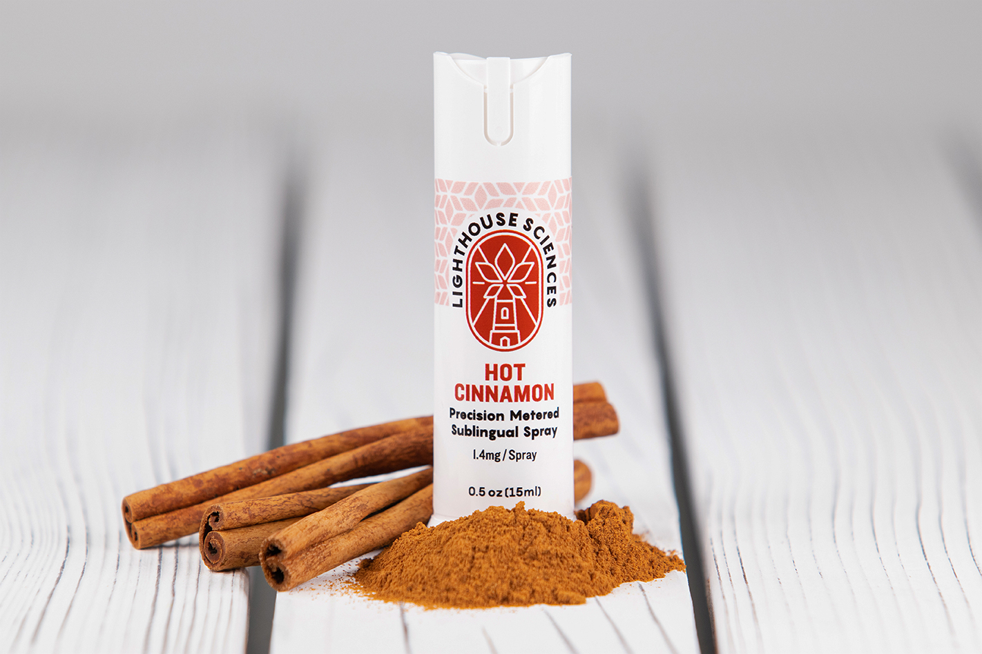 Lighthouse Sciences Hot Cinnamon- Precision Metered Sublingual Spray Bottle surrounded by cinnamon spice and cinnamon stocks on a wood background