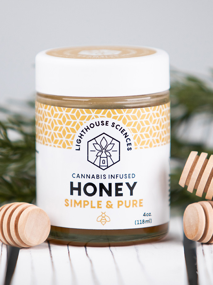 Lighthouse Sciences Cannabis Infused Honey - Simple & Pure sitting on a wood background with wood honey stirers
